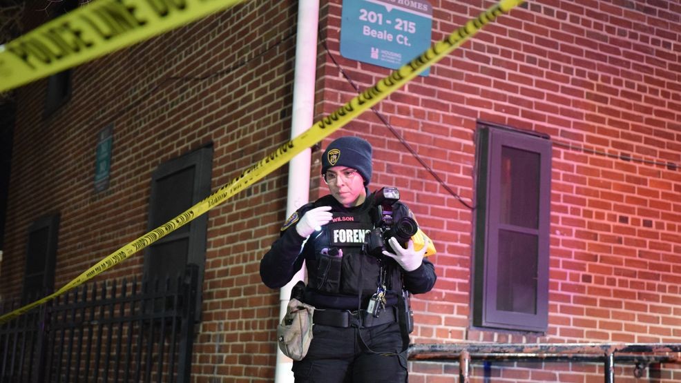 A BPD crime lab technician examines splotches of blood on the sidewalk next to the Douglass Homes affordable housing community. (WBFF / Maggie Ybarra){p}{/p}