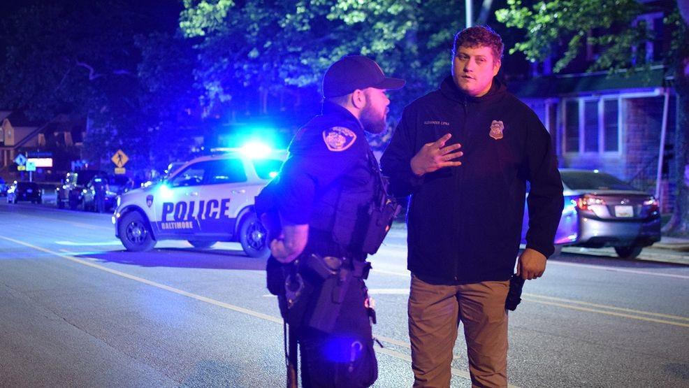 An officer talks to a detective about a shooting that shut down a main thoroughfare in northeast Baltimore. (WBFF / Maggie Ybarra)