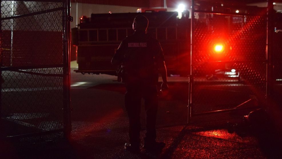 A Baltimore police officer stands at the entrance to a gated area where multiple food trucks are parked following a fire behind Patapsco Market on Thursday night. (WBFF / Maggie Ybarra)