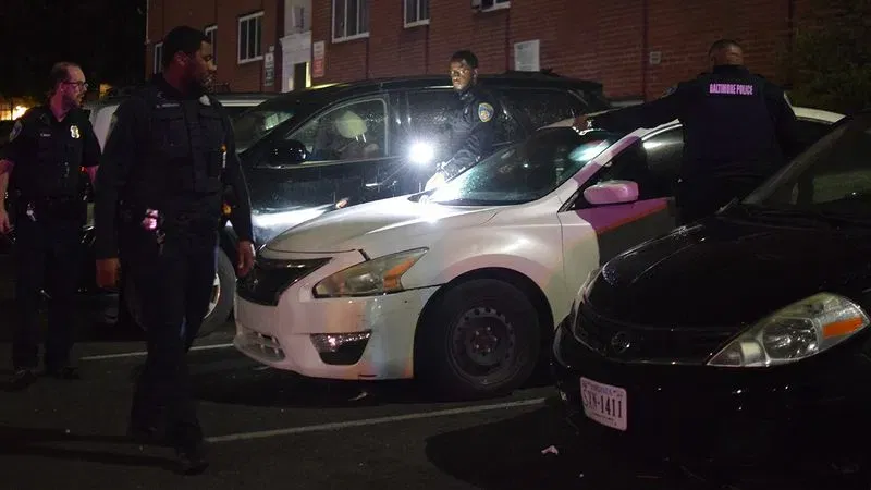 Baltimore police search the vehicles parked at the Pedestal Gardens apartment community following a burst of gunfire in west Baltimore on Wednesday. (WBFF / Maggie Ybarra)